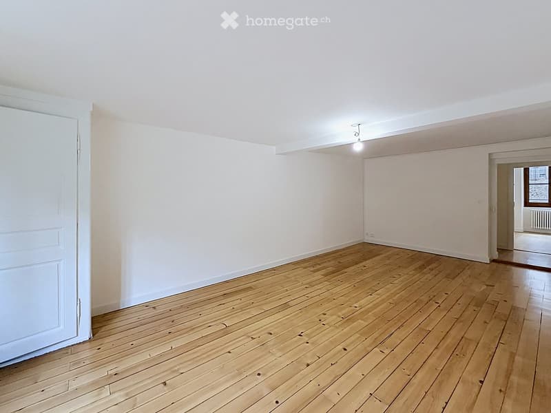 Empty room with wooden flooring and white walls, featuring a single door and a visible light fixture on the ceiling.