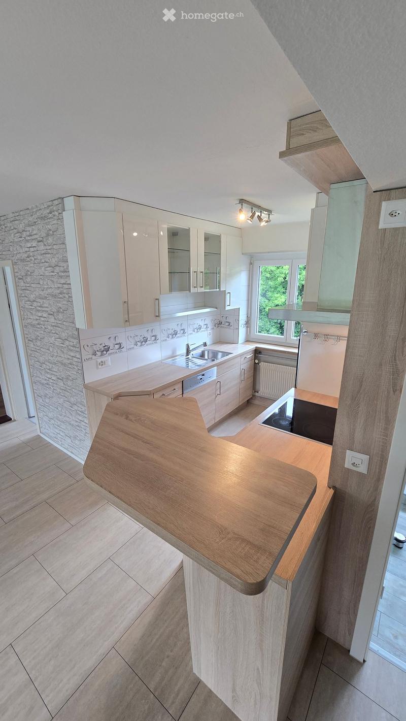 Modern kitchen with light wooden cabinets, a central island, and a stone accent wall. Features include an induction stove, sink, and ample storage space.