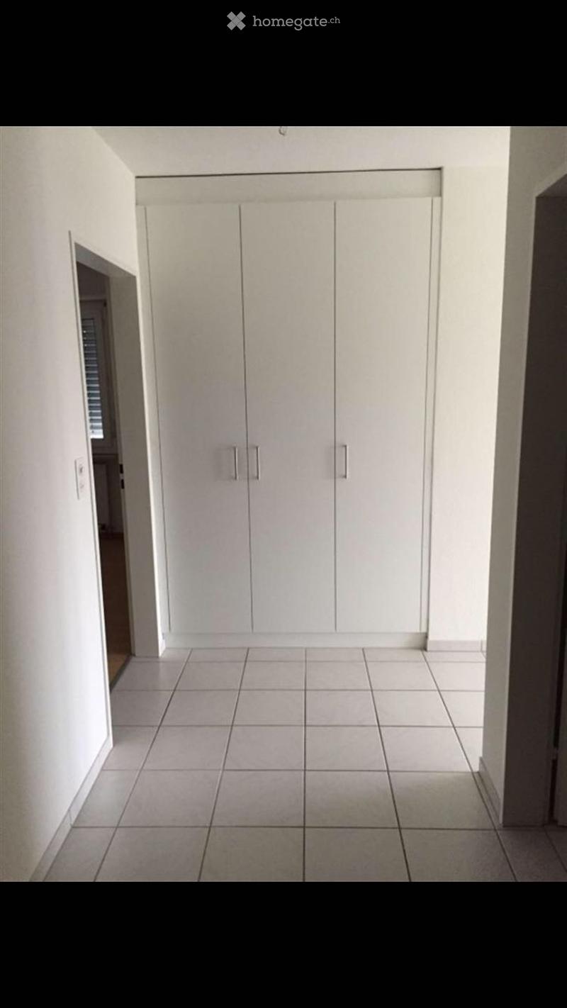 Empty hallway with white tiled flooring and white built-in closet doors.