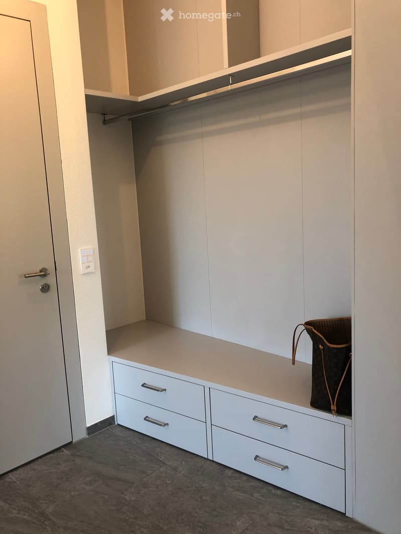 A modern, minimalist walk-in closet with white cabinetry, multiple drawers, and a single handbag placed on the shelf.