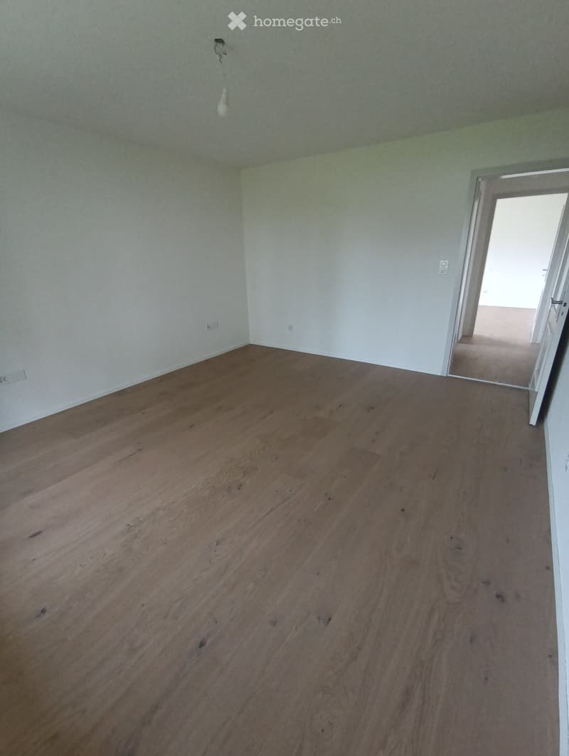 Empty room with wooden flooring and white walls, featuring a doorway leading to another space.