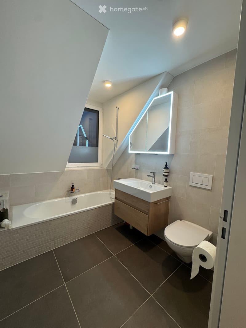 Modern bathroom with a bathtub, sink, toilet, illuminated mirror, and sleek fixtures.