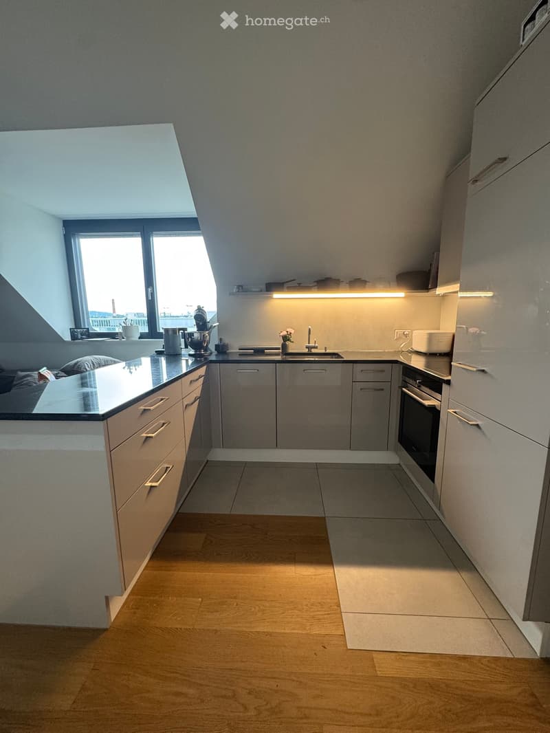 Modern kitchen with light grey cabinets, wooden floor, and a large window. Features a sink, oven, and various appliances.