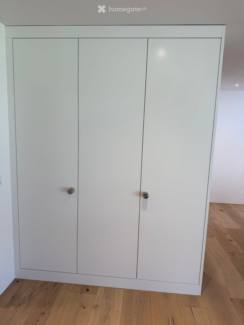 Empty room with light-colored cabinetry and wooden flooring.