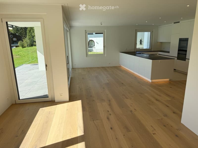 Empty kitchen with light wooden flooring, white cabinets, and a black countertop. Large windows and a sliding glass door lead to an outdoor area.