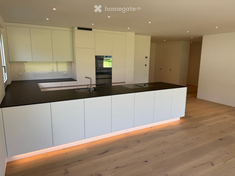Modern kitchen with white cabinets, black countertops, a central island, and a sink with a faucet. The floor is made of light wooden planks.