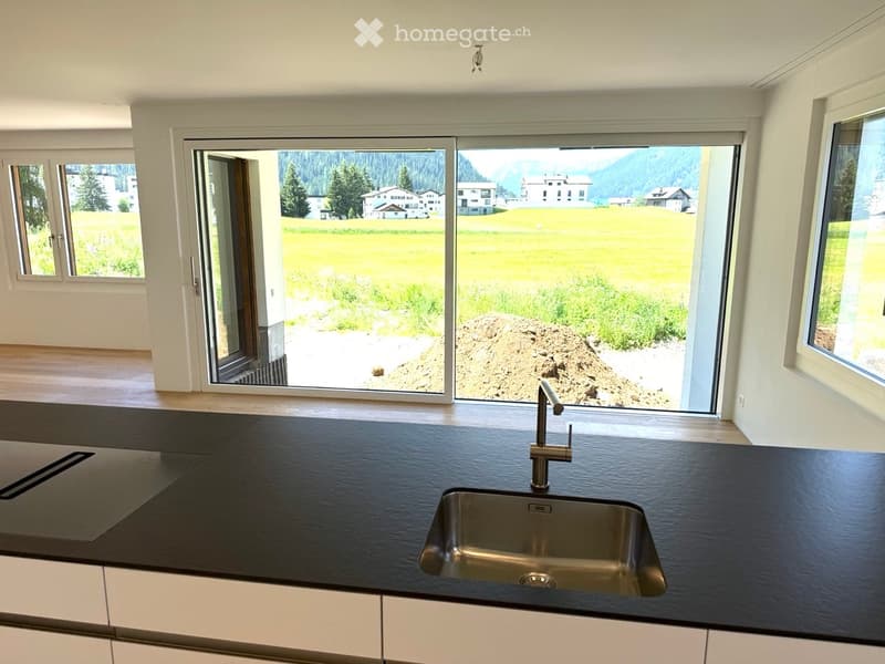 Modern kitchen with black countertop, stainless steel sink, and large windows offering a scenic view of a green field and distant mountains.