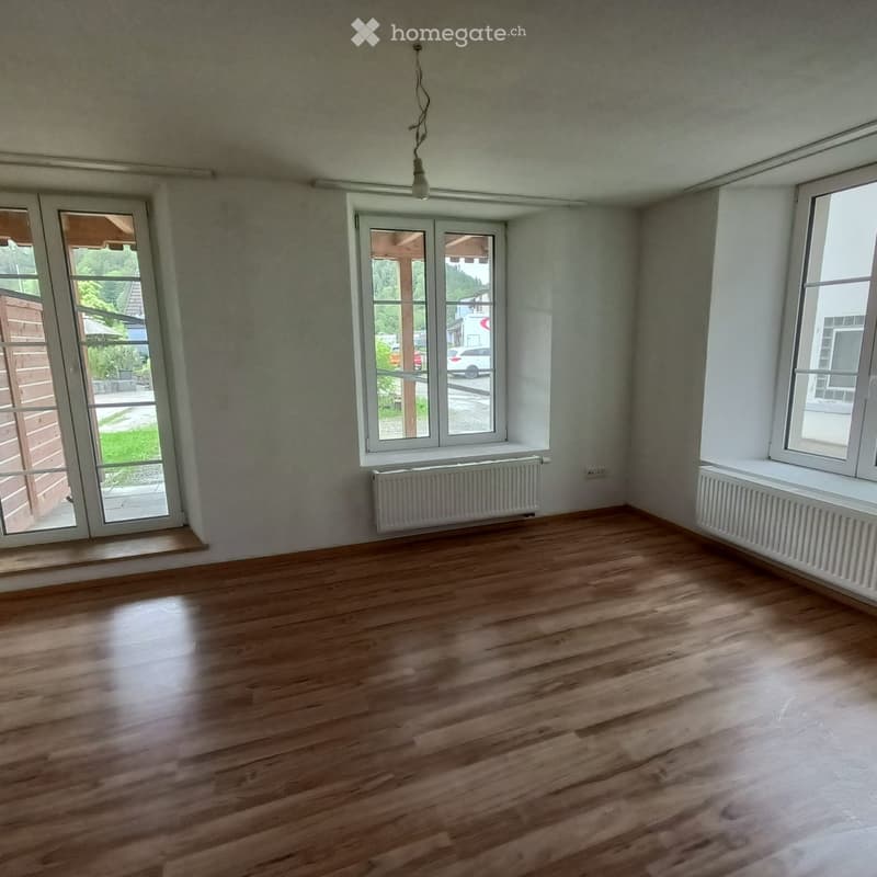 Empty room with wooden flooring, white walls, large windows, and radiators. No furniture or equipment present.