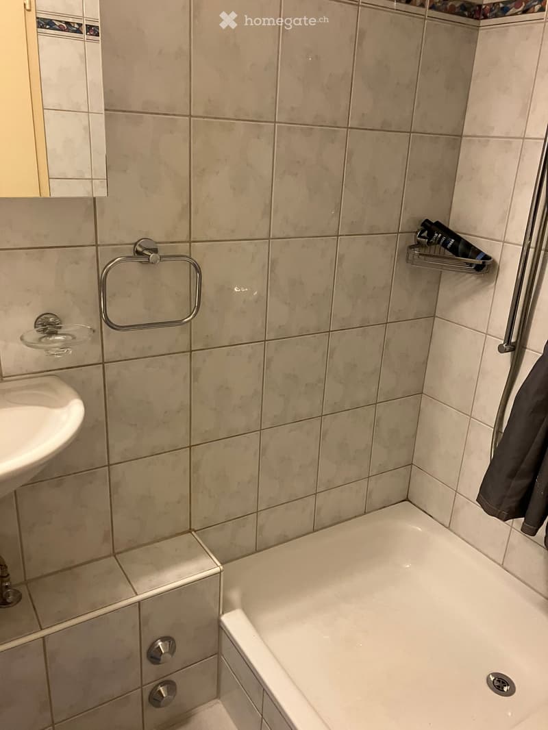 Bathroom with a white bathtub, a sink, a mirror, a towel rack, and a towel hanging on the side.