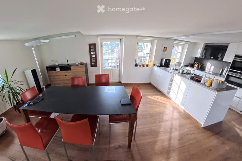 Open-plan kitchen and dining area with white cabinets, a black dining table with red chairs, and a modern kitchen setup.