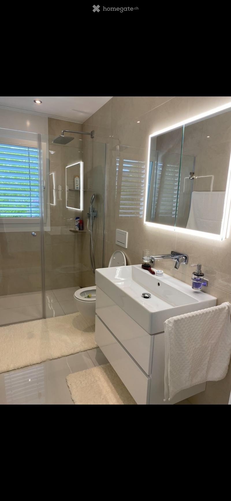 Modern bathroom with a white sink, mirror with LED lighting, toilet, glass-enclosed shower, and towel on a cabinet.