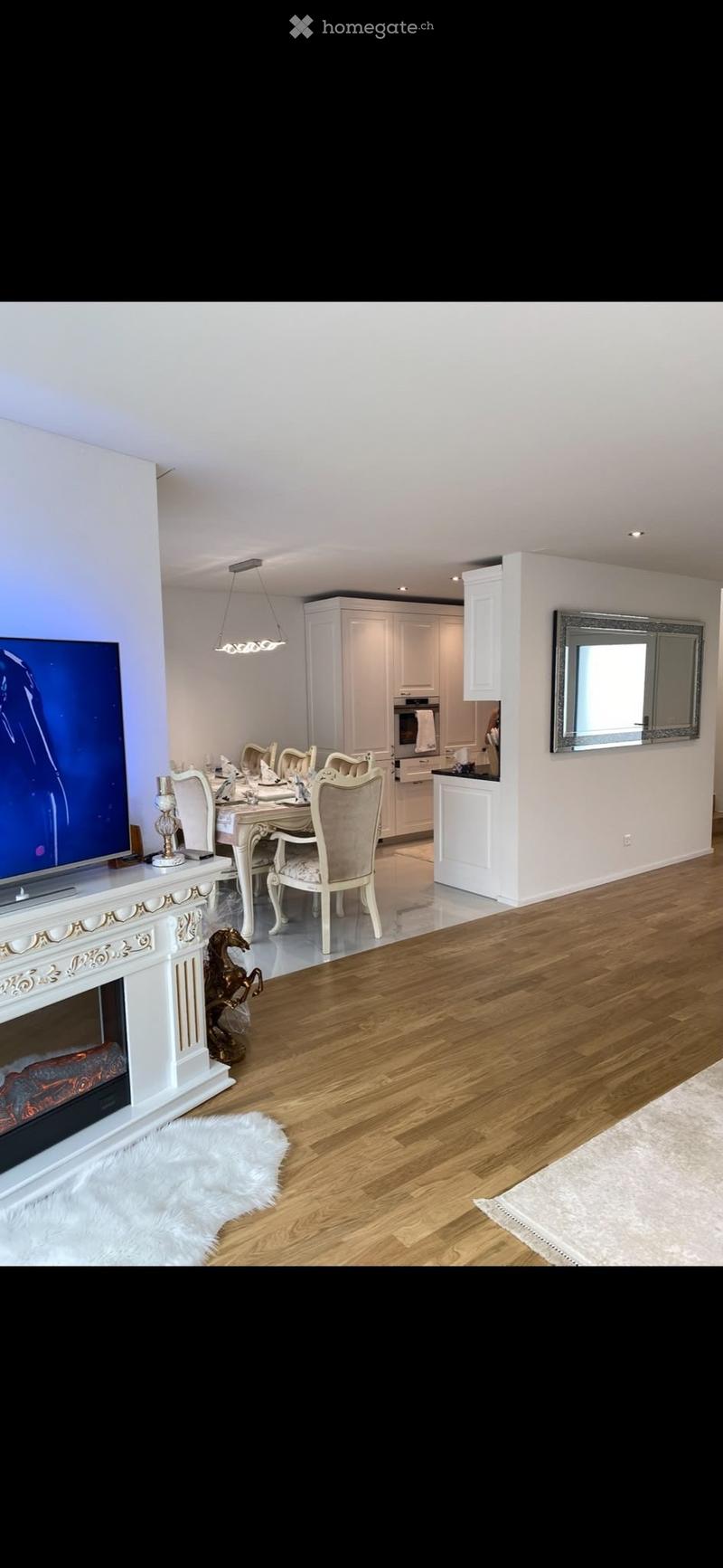 Open-concept living and dining area with hardwood floors, a fireplace, a dining set, and a modern kitchen in the background.