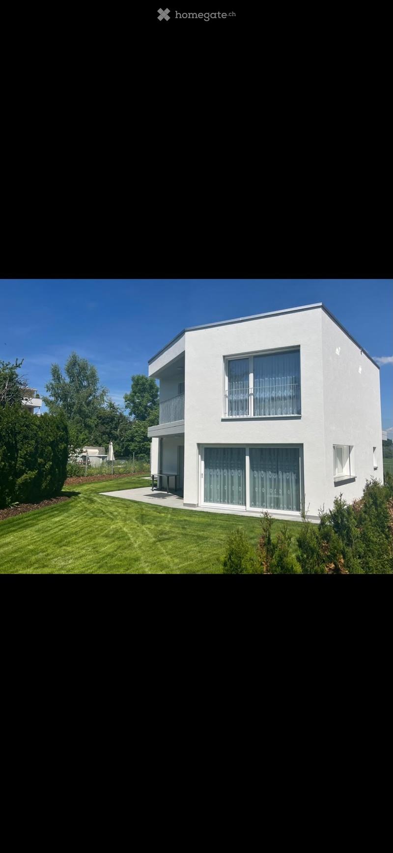 Modern two-story white house with large windows, balcony, and well-maintained lawn.