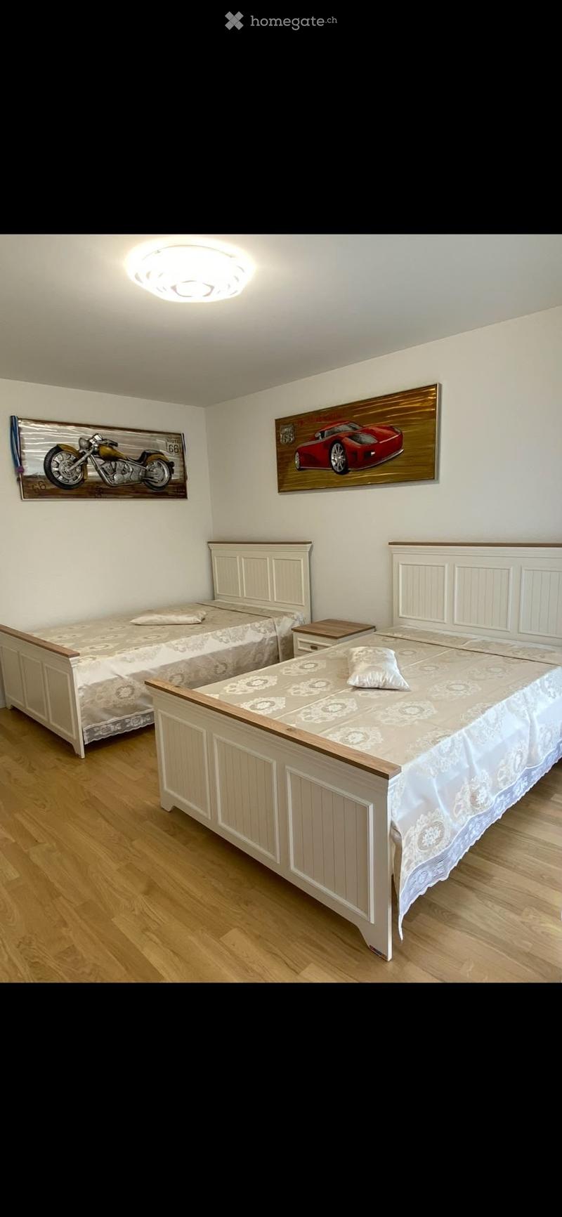 Cozy bedroom with two single beds, wooden nightstands, and decorative wall art featuring a motorcycle and a sports car.