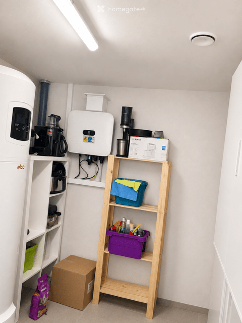 Utility room with a refrigerator, microwave, coffee maker, water heater, and shelves holding storage boxes and cleaning supplies.