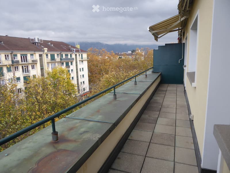 Balcony with tiled floor, metal railing, and view of trees and buildings.