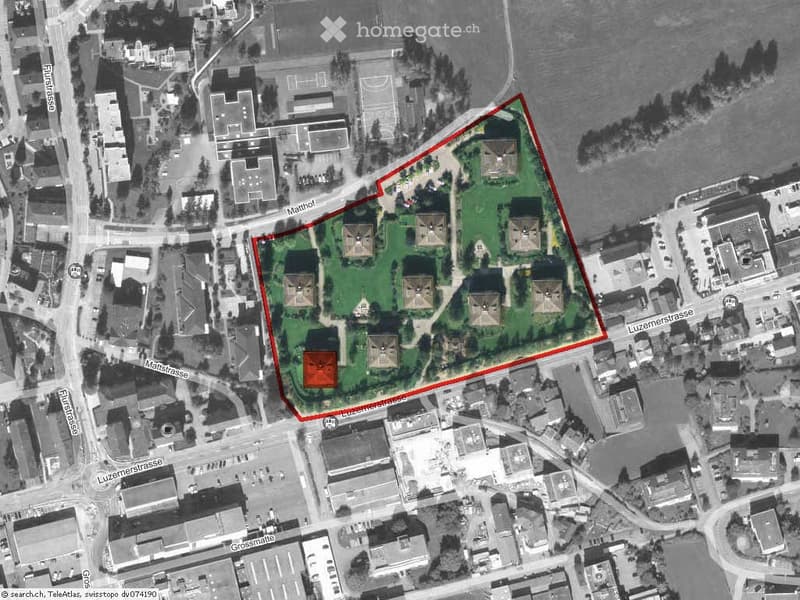 Aerial view of a large building complex surrounded by green spaces and located near a body of water, with multiple structures and pathways visible.