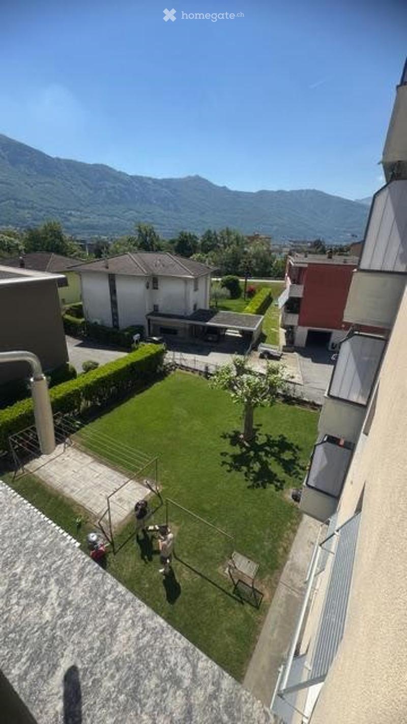 A well-maintained garden with a grassy lawn, a small tree, and a playground area, overlooking a scenic mountain view.