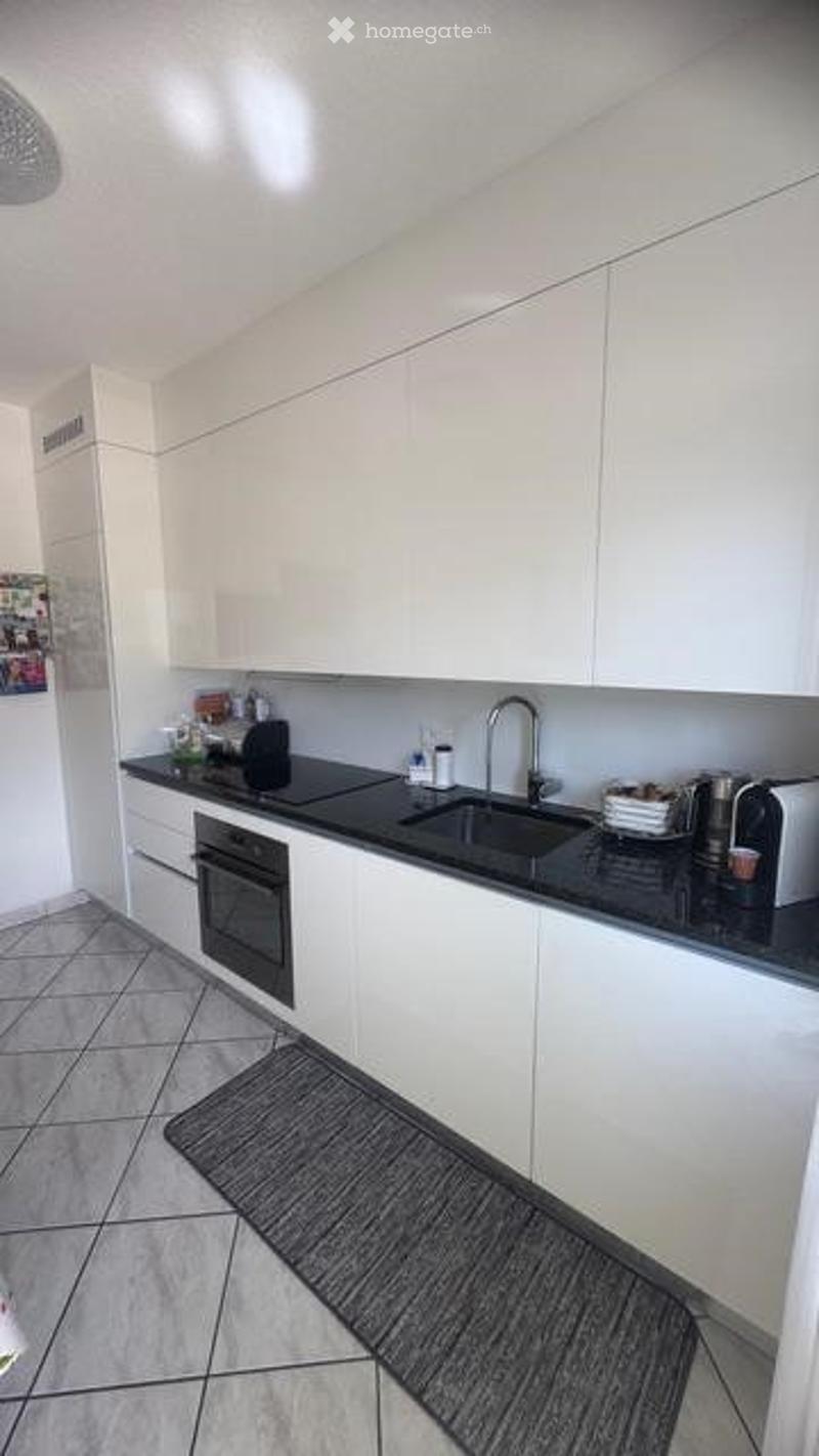 Modern kitchen with white cabinets, black countertops, and stainless steel appliances including an oven, sink, and coffee maker.