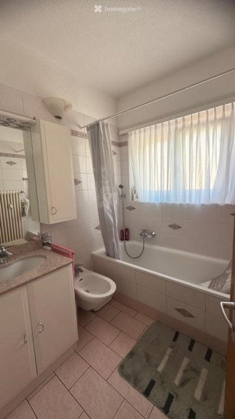 Bathroom with a sink, mirror, cabinet, bathtub, shower curtain, and toilet. The space features tiled walls and floor, a window with a curtain, and a radiator.