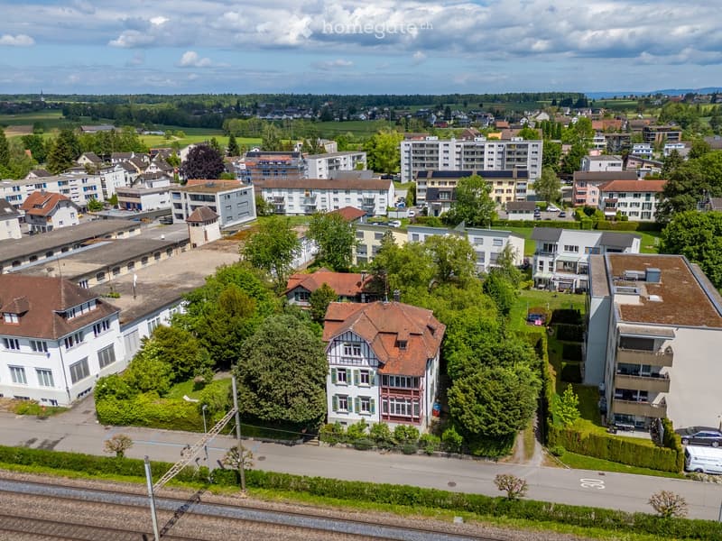 Aerial view of a residential area with a mix of apartment buildings and single-family homes, surrounded by greenery and trees.