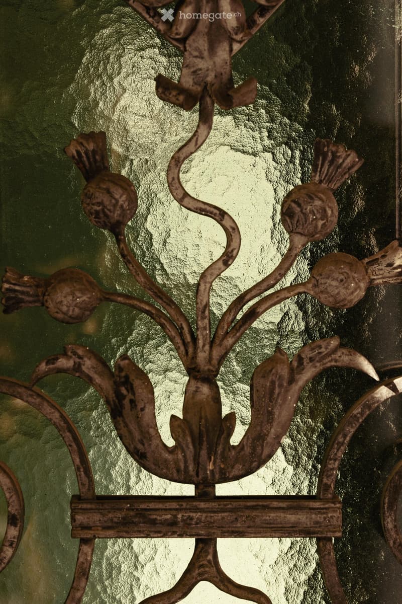 An ornate metal railing with intricate scrollwork and decorative finials, mounted on a green wall.