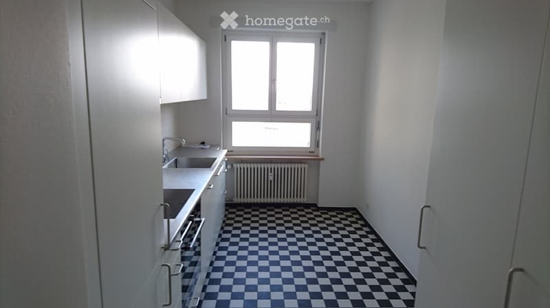 Empty kitchen with white cabinets, a sink, a window, and a checkered black and white floor.