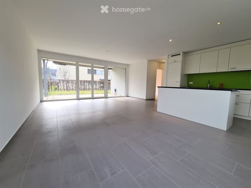 Empty room with tiled floor, white walls, large sliding glass doors leading to outdoor area, and a small kitchen area with cabinets and countertop.