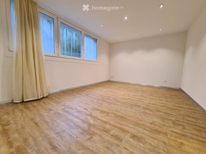 Empty room with wooden flooring, white walls, and large windows with curtains.