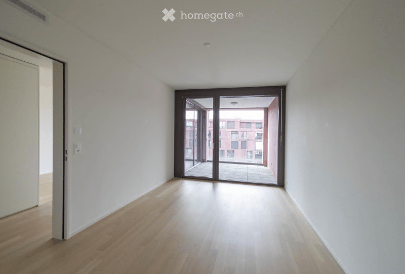 Empty room with light wooden flooring, white walls, and large sliding glass doors leading to a balcony area.
