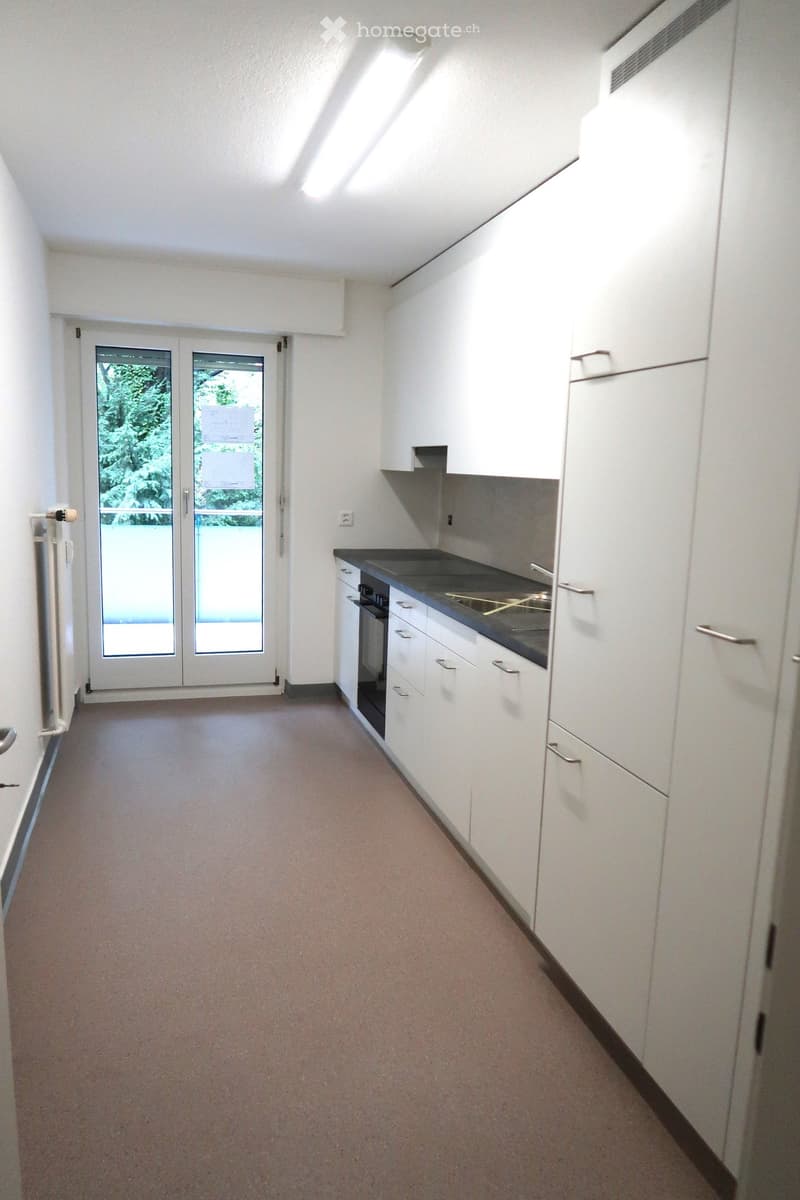 Empty kitchen with white cabinets, black countertop, and a double glass door leading outside.