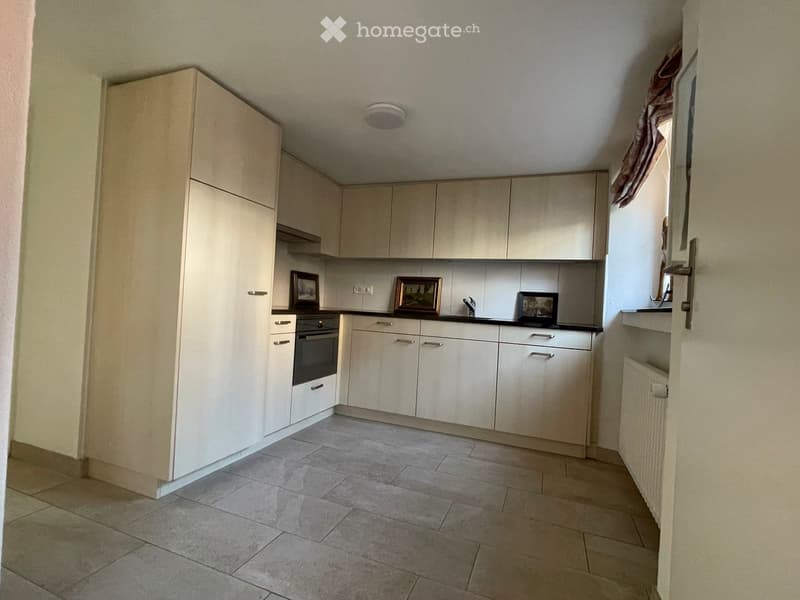 Modern kitchen with light-colored cabinets, tiled floor, and a built-in oven. The countertop features a few decorative items and a faucet.