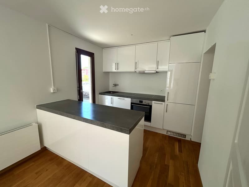 Modern kitchen with white cabinets, a black countertop, and built-in appliances including a refrigerator, oven, and sink. The floor is wooden, and there is a door leading outside.