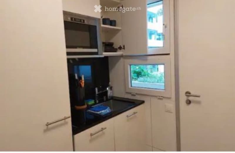 Modern kitchen with white cabinets, black countertop, microwave, oven, and sink. Features a window with a view of greenery.
