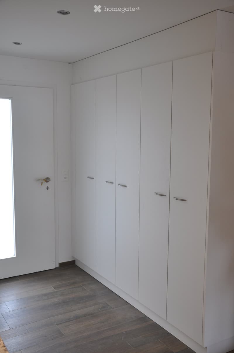 Empty room with white built-in wardrobes, wooden flooring, and a small window near the door.