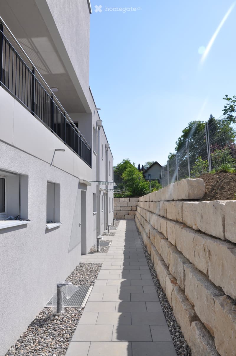 Modern corridor with tiled flooring, stone retaining wall, and metal railing on the left side.