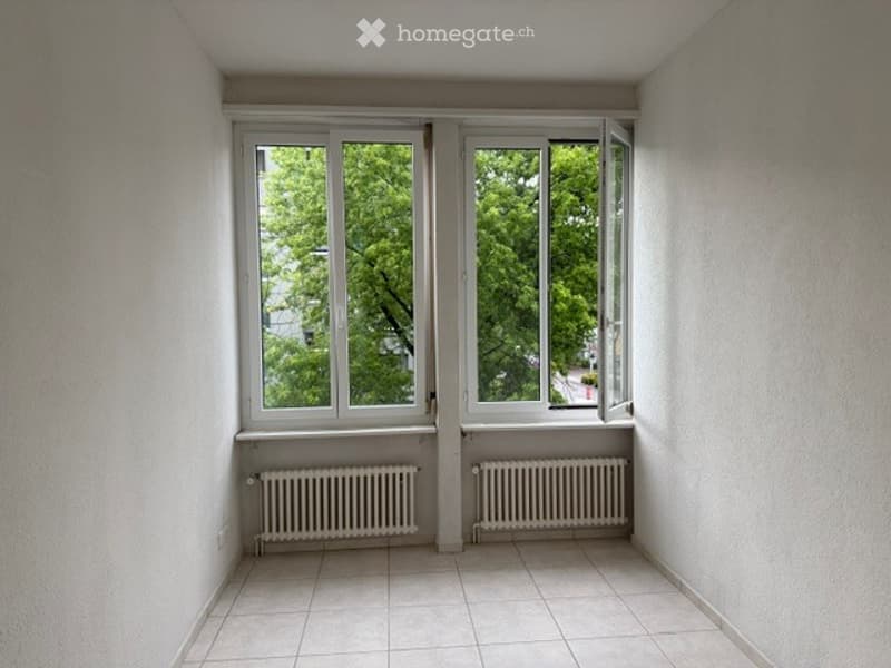 Empty room with white tiled floor, white walls, two large windows with white frames, and two radiators beneath the windows.