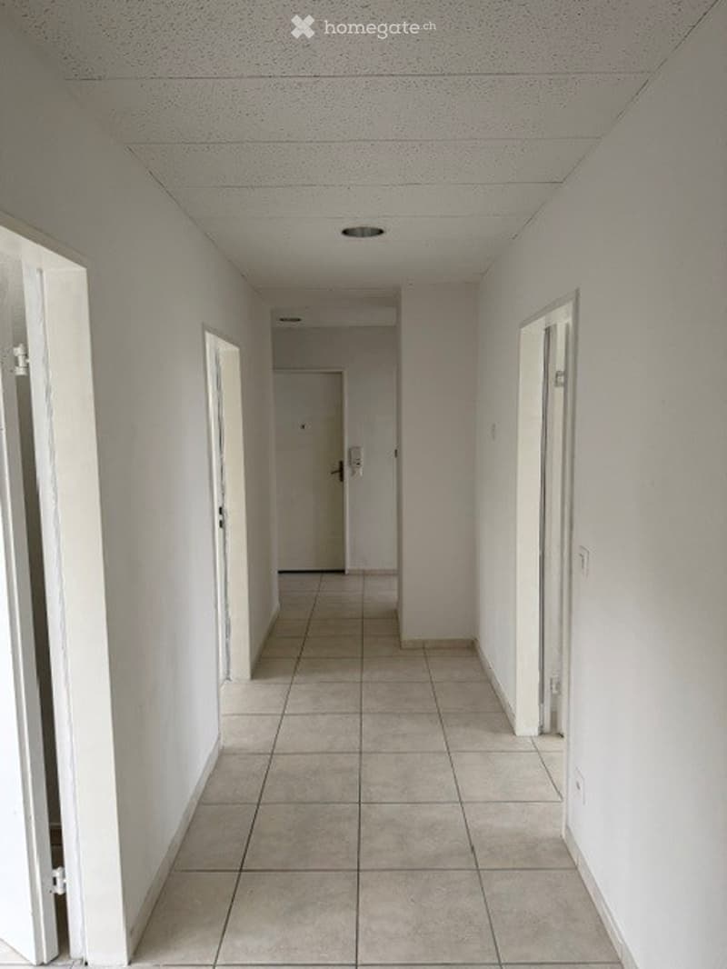 Empty hallway with white walls, tiled floor, and several doors.