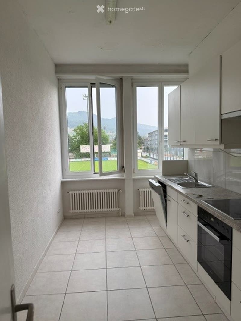 Modern kitchen with white cabinets, tiled floor, large windows offering a view of the landscape, sink, oven, and dishwasher.
