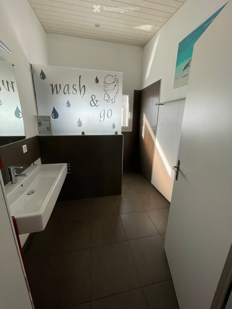 Modern bathroom with a white sink, chrome faucet, dark tiled backsplash, and a decorative wall sign reading "wash & go".