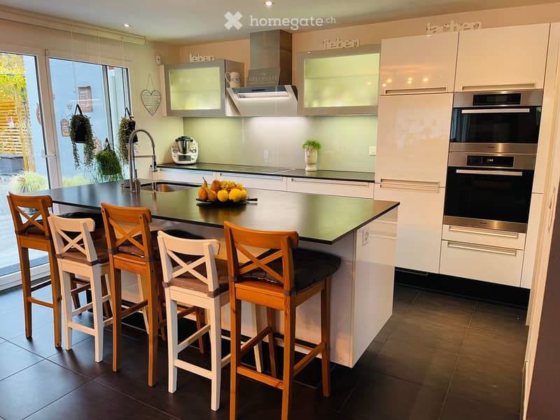 Modern kitchen with white cabinets, island, bar stools, and stainless steel appliances.