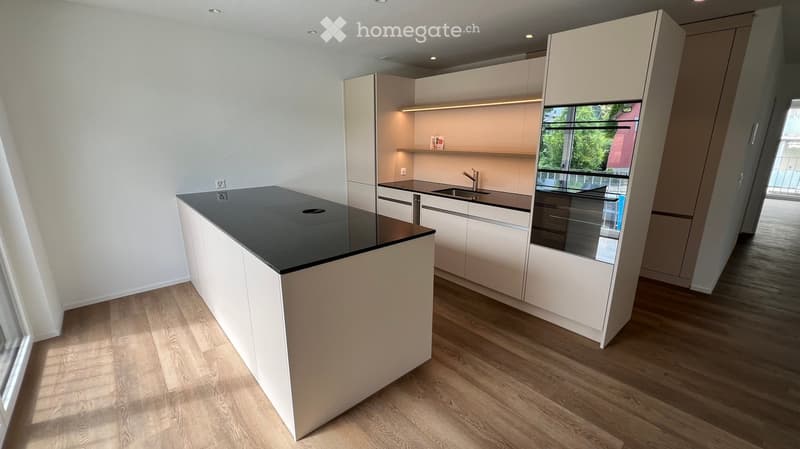 Modern kitchen with white cabinets, a black countertop island, and a sink area. The floor is wooden, and the space is well-lit with recessed lighting.