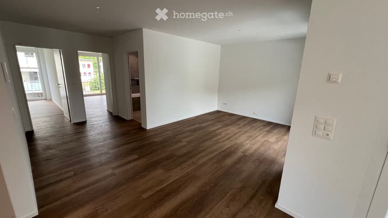 Empty room with light wooden flooring and white walls, featuring an open doorway leading to a balcony area.