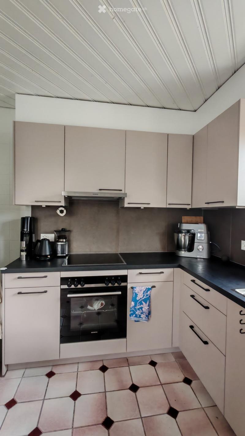 Modern kitchen with light-colored cabinets, stainless steel appliances, and a black countertop. Features include an oven, coffee maker, and a towel hanging on a cabinet handle.