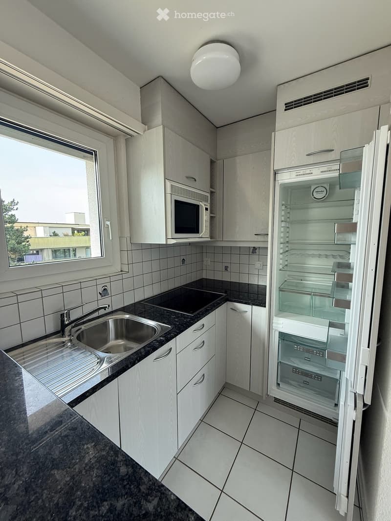 Modern kitchen with white cabinets, granite countertop, stainless steel sink, microwave, and open refrigerator.