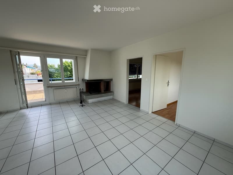 Empty room with white tiled floor, white walls, fireplace, radiator, and large windows with a view of the outside.