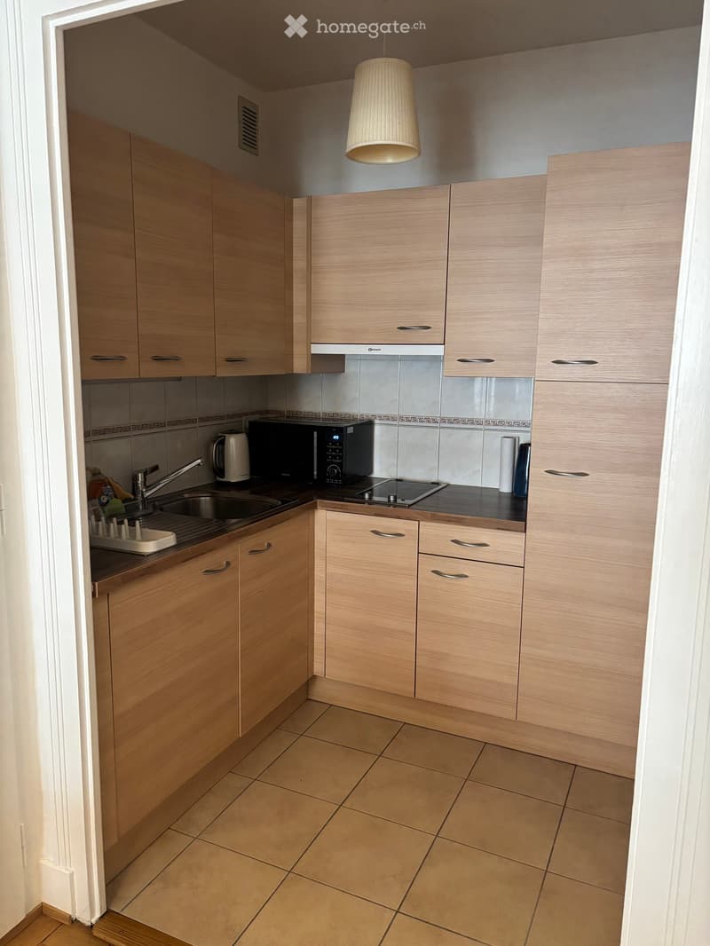 Modern kitchen with light wood cabinets, tiled backsplash, and stainless steel appliances including a microwave and electric kettle.