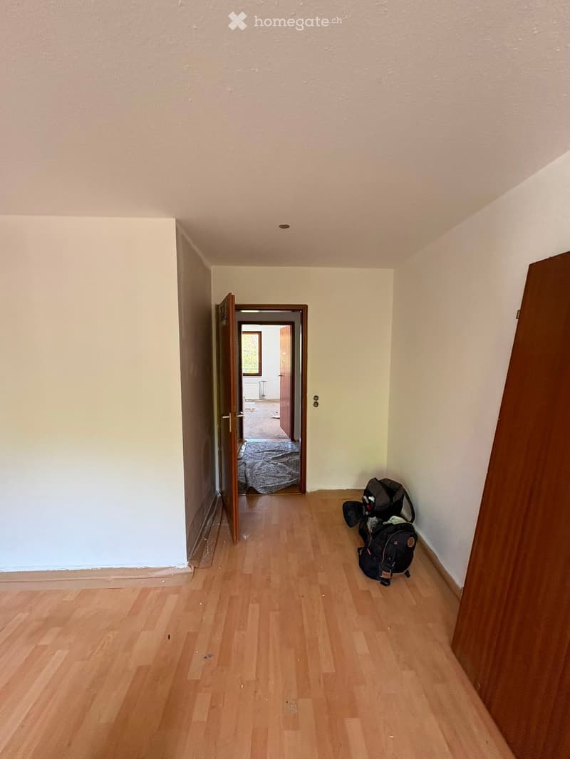 Empty hallway with wooden flooring, white walls, and a partially open door leading to another room.