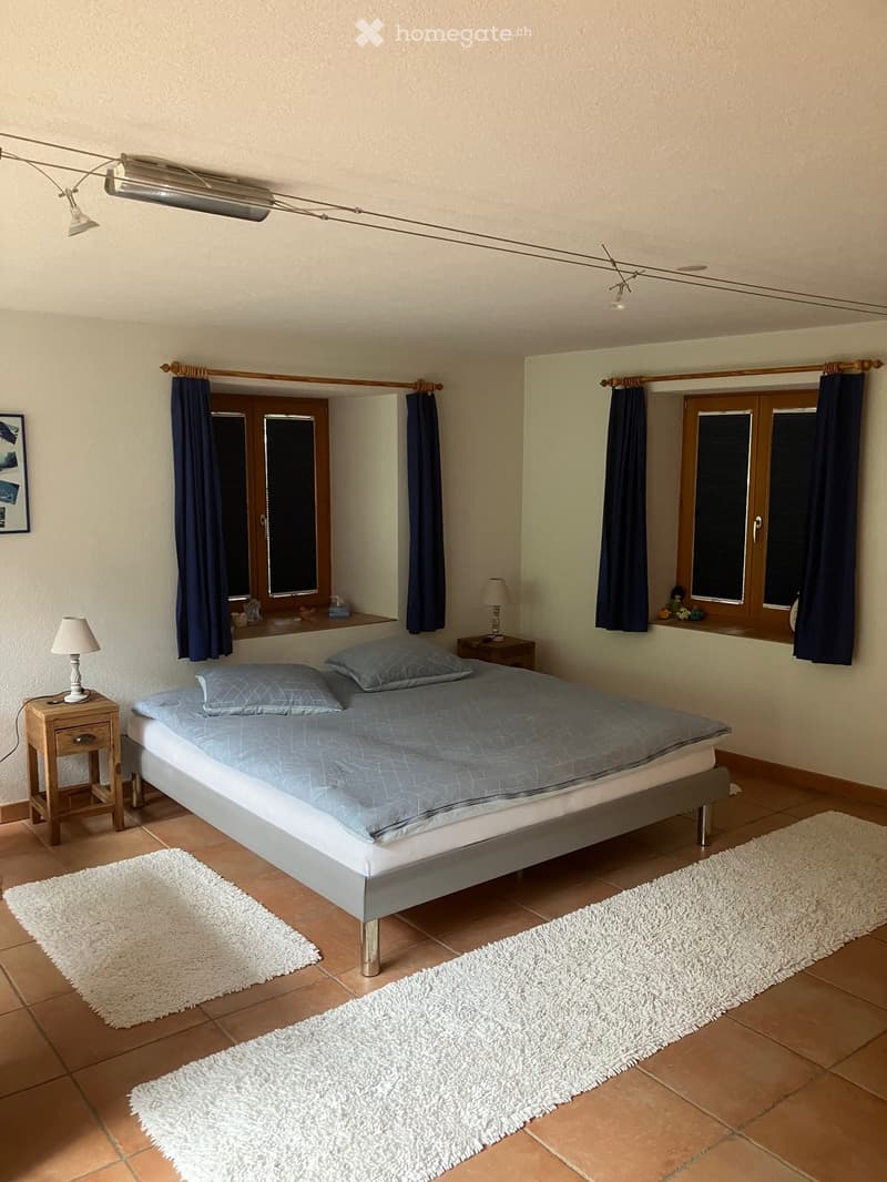 Cozy bedroom with a double bed, nightstands, lamps, and rugs on a tiled floor.