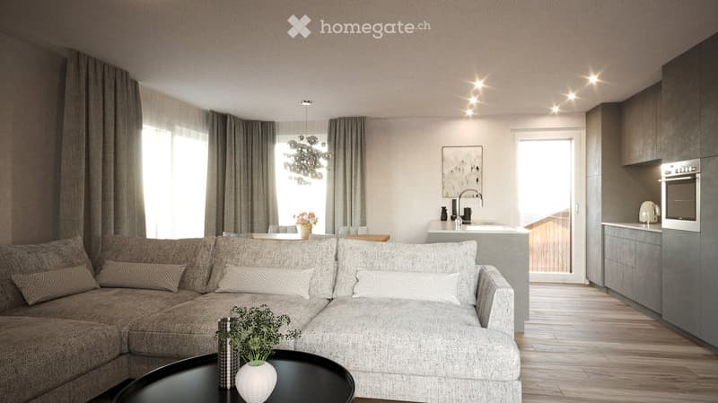 Modern living room with a grey sectional sofa, coffee table, vase with greenery, and a small kitchen area with cabinets, sink, and oven. Large windows with curtains and a chandelier are visible.